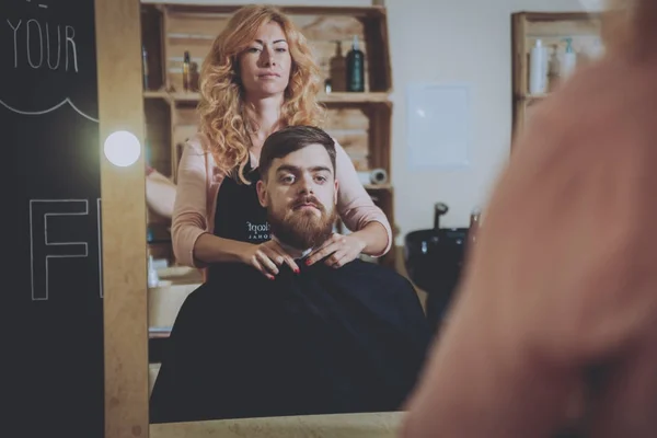 Master cuts hair and beard of men, hairdresser makes hairstyle for a young man.