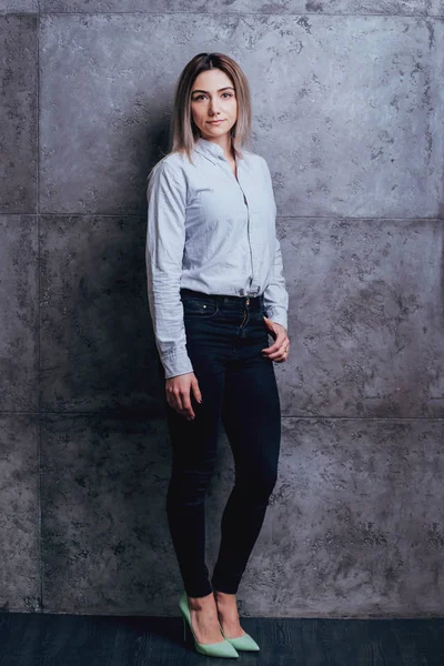 Attractive caucasian woman dressed in shirt posing before grey wall