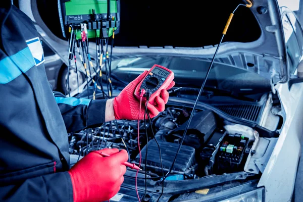 Auto mechanic uses a voltmeter to check the voltage level. Car repair. Service station.