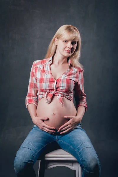 工作室图片美丽的怀孕的金发女郎在格子衬衫和蓝色牛仔裤 — 图库照片