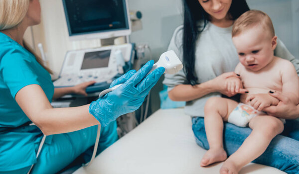 Doctor and infant girl with mother at ultrasound diagnosis. Medical equipment. Sonography.