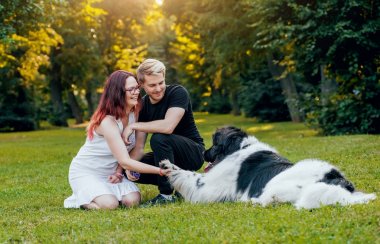 Genç çift yeşil park ile siyah ve beyaz Newfoundland köpek çalış
