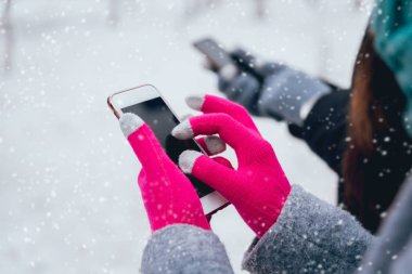 Smartphone ile pembe eldiven dokunmatik ekranlar için kışın kullanan kadın.