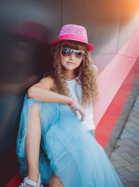 Küçük kız pembe şapka ve süslü mavi etek sokakta poz
