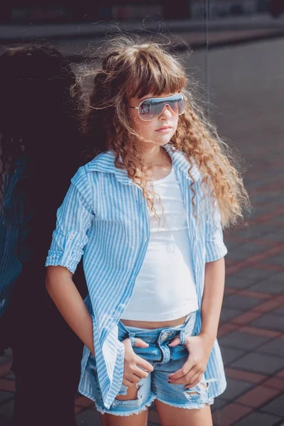 Sokakta poz yaz kıyafeti ve güneş gözlüklü küçük kız.