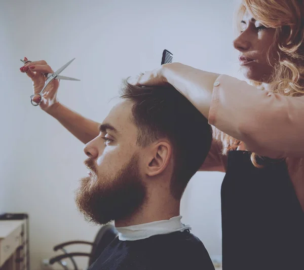 Master cuts hair and beard of men, hairdresser makes hairstyle for a young man.