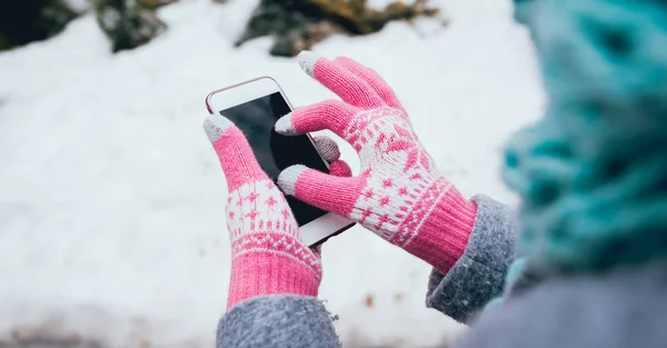 Woman using smartphone with pink gloves for touch screens in winter.