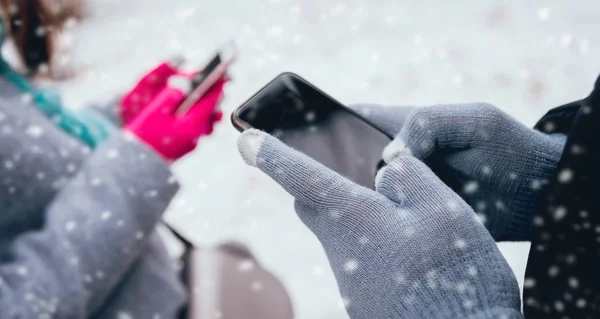 Couple using smartphone with gloves for touch screens in winter