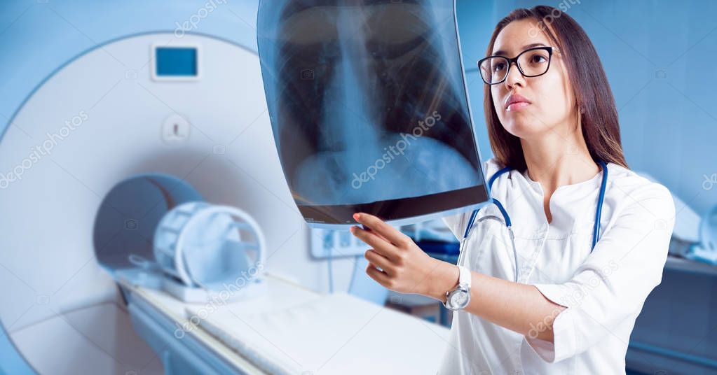 Young female doctor looking at an x-ray film in hospital room.