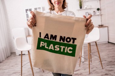 Elinde bez bir çanta tutan genç bir kız. Mutfakta. Ben plastik değilim. Plastik poşet kullanımını azaltma kampanyası. Sıfır atık