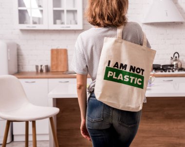 Elinde bez bir çanta tutan genç bir kız. Mutfakta. Ben plastik değilim. Plastik poşet kullanımını azaltma kampanyası. Sıfır atık