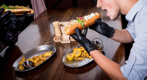 Deux jeunes hommes affamés mangeant des hot-dogs dans un café. Restaurant — Photo