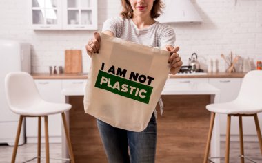 Elinde bez bir çanta tutan genç bir kız. Mutfakta. Ben plastik değilim. Plastik poşet kullanımını azaltma kampanyası. Sıfır atık