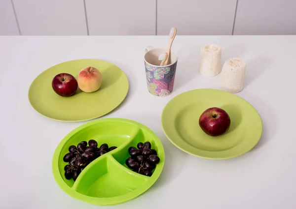 Bamboe tandenborstels, washandjes, kopjes en borden op de witte tafel in de keuken. Geen afval — Stockfoto