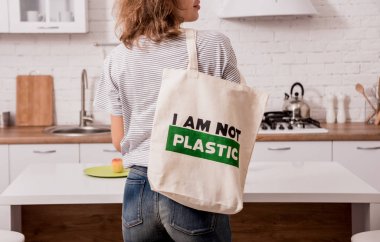 Elinde bez bir çanta tutan genç bir kız. Mutfakta. Ben plastik değilim. Plastik poşet kullanımını azaltma kampanyası. Sıfır atık