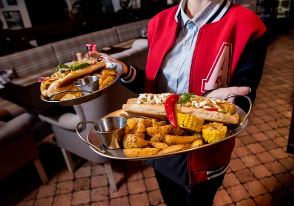 Číšník s dvěma talíři s velkým párkem a hranolkama. Restaurace. — Stock fotografie