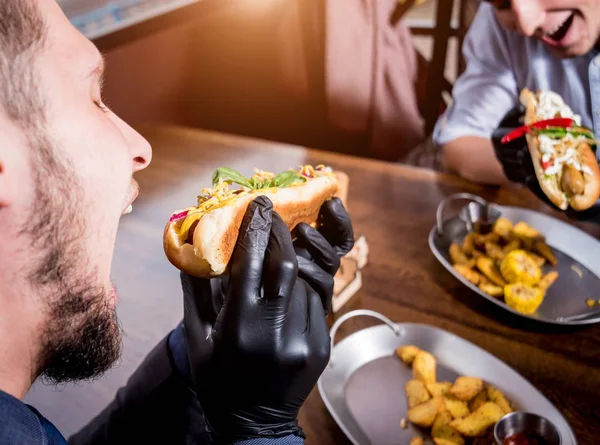 Dva hladoví mladí muži jedí hot dogy v kavárně. Restaurace — Stock fotografie