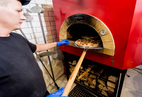 Le processus de fabrication de la pizza. Chef boulanger met la pizza crue dans le four. Cuisine . — Photo