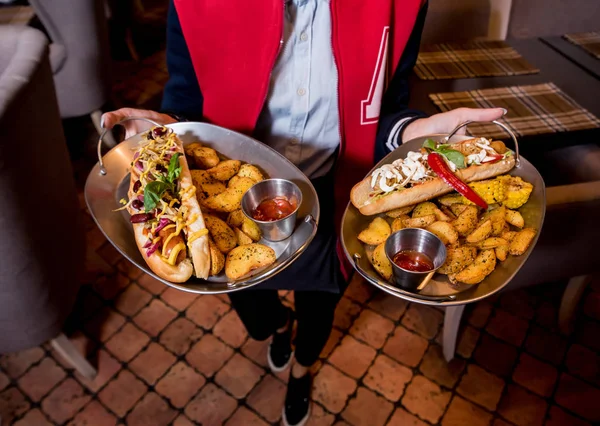 Číšník s dvěma talíři s velkým párkem a hranolkama. Restaurace. — Stock fotografie