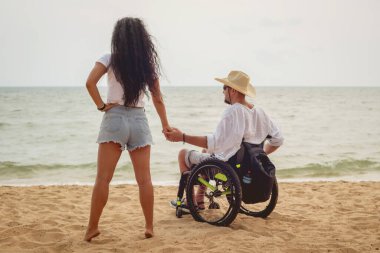 Disabled man in a wheelchair with his wife on the beach.