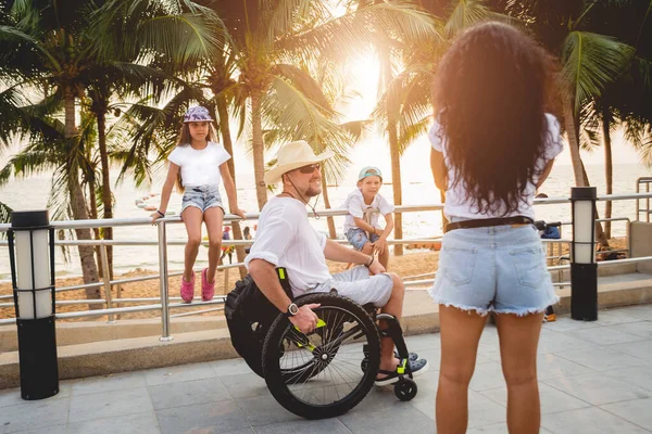 Hombre discapacitado en silla de ruedas con su familia en la playa . —  Fotos de Stock