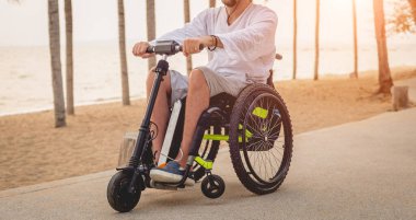 Disabled man in a wheelchair with electric scooter on the beach