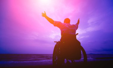 Disabled man in a wheelchair on the beach. Silhouette at sunset.