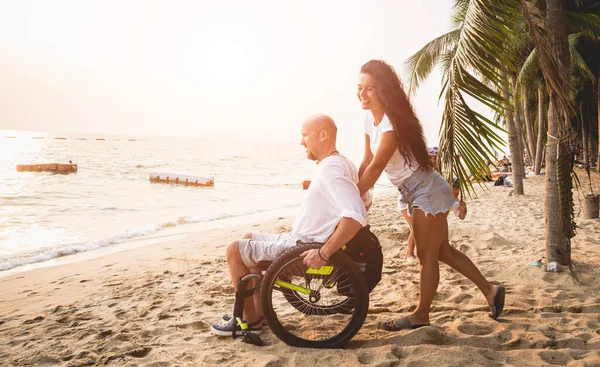 Disabled man in a wheelchair with his wife on the beach. — Stock fotografie