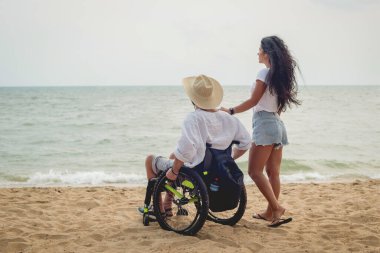 Disabled man in a wheelchair with his wife on the beach.