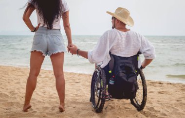 Disabled man in a wheelchair with his wife on the beach.
