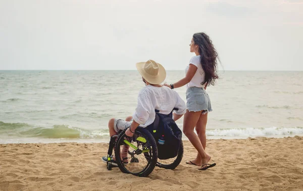 Homem deficiente em uma cadeira de rodas com sua esposa na praia . — Fotografia de Stock