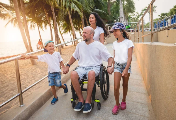 Disabled man in a wheelchair moves on a ramp to the beach with his family. — 스톡 사진