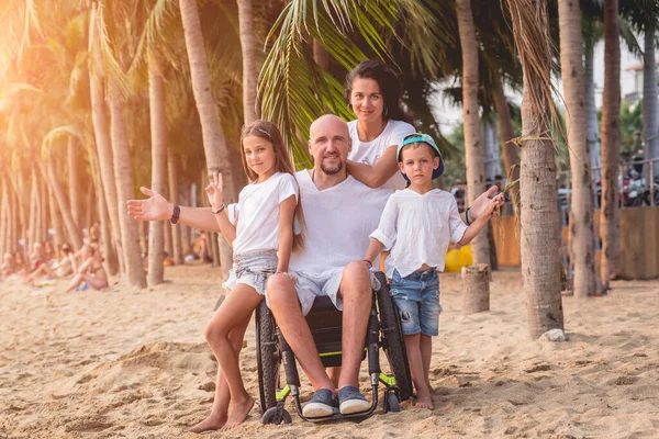 Homem deficiente em uma cadeira de rodas com sua família na praia . — Fotografia de Stock