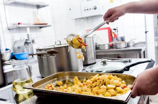 Chef cooks fried potatoes with pieces of meat in a restaurant kitchen