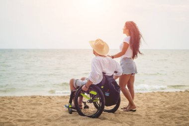 Disabled man in a wheelchair with his wife on the beach.