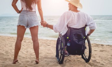 Disabled man in a wheelchair with his wife on the beach.