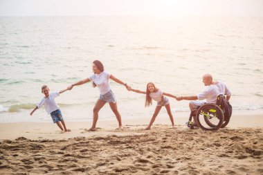 Disabled man in a wheelchair with his family on the beach.