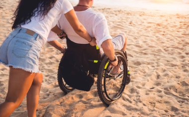 Disabled man in a wheelchair with his wife on the beach.
