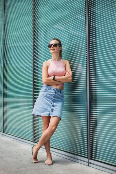 Young sexy woman in sunglasses posing near glass wall. — Stock Photo, Image