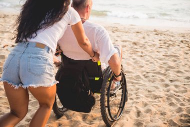 Disabled man in a wheelchair with his wife on the beach.
