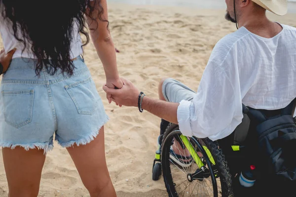 Homem deficiente em uma cadeira de rodas com sua esposa na praia . — Fotografia de Stock