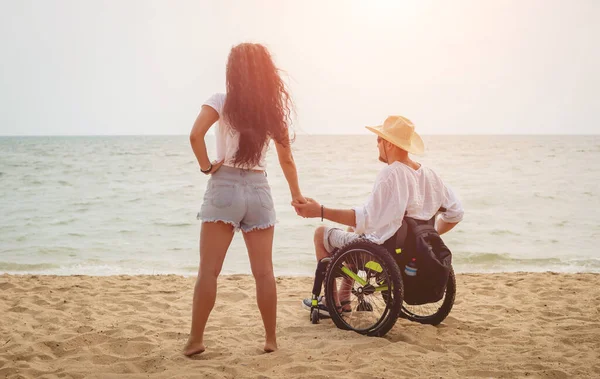 Disabled man in a wheelchair with his wife on the beach.