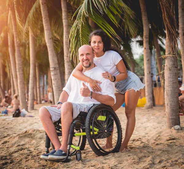 Homem deficiente em uma cadeira de rodas com sua esposa na praia . — Fotografia de Stock