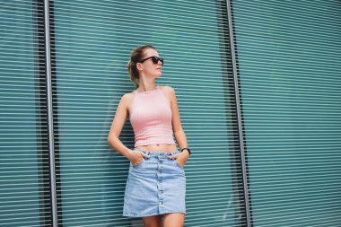 Güneş gözlüklü genç seksi kadın cam duvarın yanında poz veriyor..