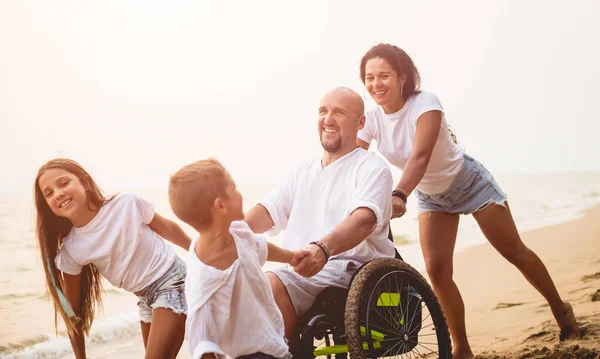 Homem deficiente em uma cadeira de rodas com sua família na praia . — Fotografia de Stock