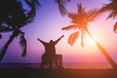 Disabled man in a wheelchair on the beach. Silhouette at sunset.