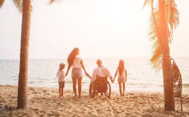 Disabled man in a wheelchair with his family on the beach.