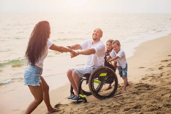 Homem deficiente em uma cadeira de rodas com sua família na praia . — Fotografia de Stock