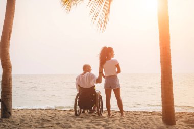 Disabled man in a wheelchair with his wife on the beach.