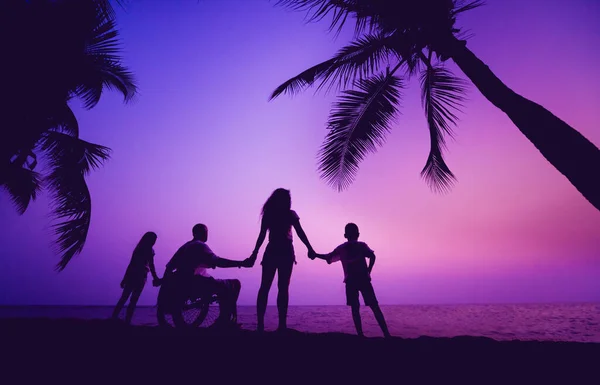 Disabled man in a wheelchair with his family on the beach. Silhouettes at sunset — Φωτογραφία Αρχείου